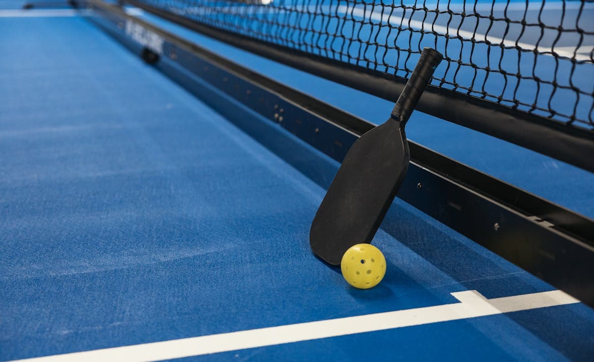 Pickleball paddle and ball leaning against net on blue court