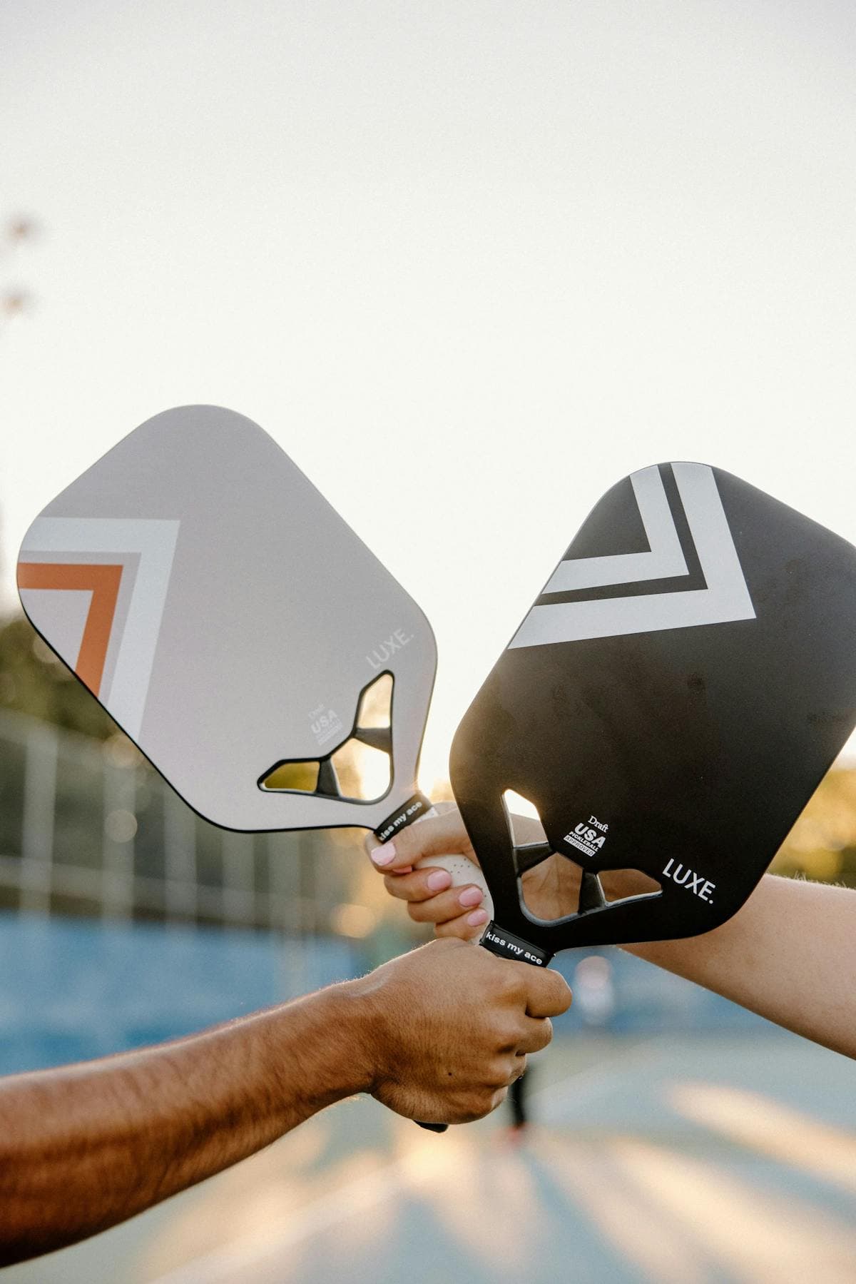 Two pickleball players holding paddles on court at sunset