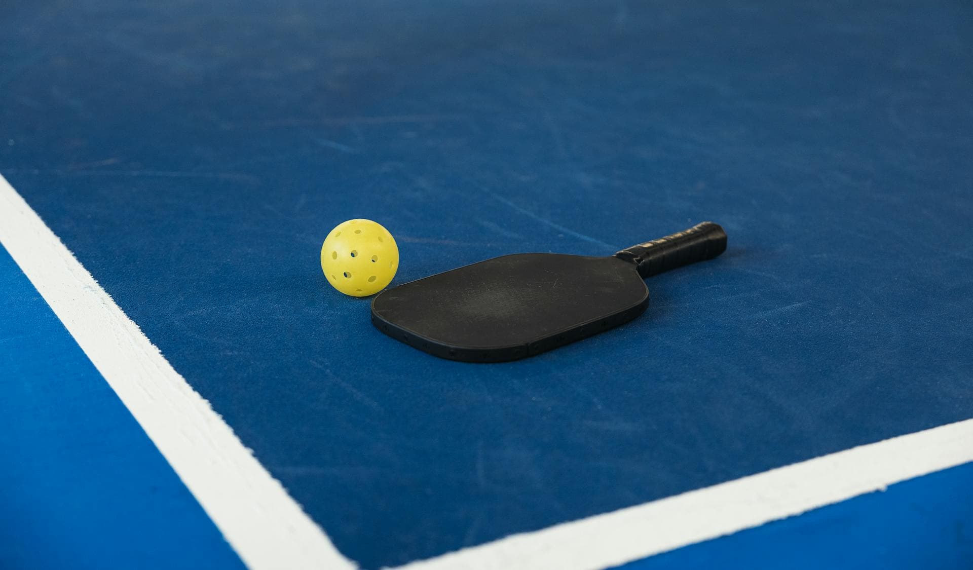 Pickleball paddle and ball on a blue court